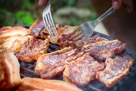 Soczysty boczek na grillu, idealny po marynacie. Dwie widelce pomagają w obracaniu kawałków.