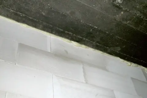 Dylatacja komina od stropu wykonana pianką montażową. Białe pustaki i ciemny strop.
