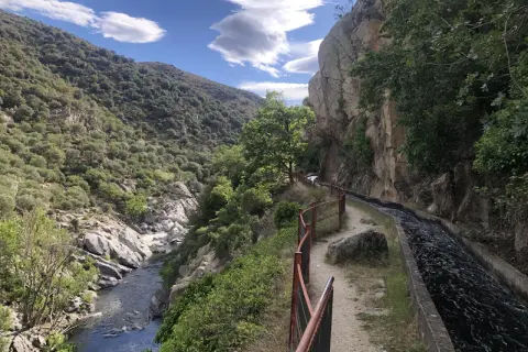 Sentier longeant un canal d'eau vive dans les gorges de la Guillera, avec une rivière en contrebas et des montagnes verdoyantes.