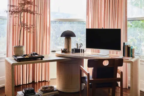 Stylish personal office decor ideas: a modern desk with a computer, lamp, and plant, framed by soft pink curtains.
