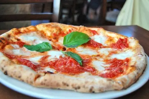 Une délicieuse margarita pizza, avec sa croûte dorée, sa sauce tomate vibrante et son fromage fondant, garnie de feuilles de basilic frais.