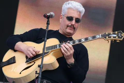 Un cantautore napoletano famoso con capelli bianchi e occhiali da sole suona una chitarra jazz.