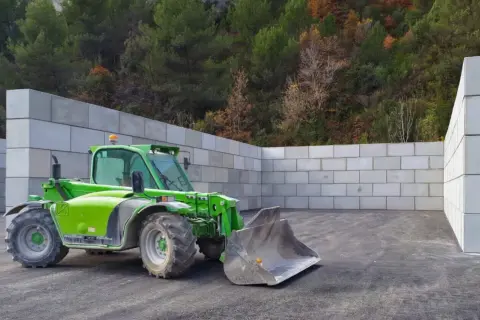 Chargeuse verte dans un espace clos de murs en blocs de béton, prêt pour le silo ensilage.