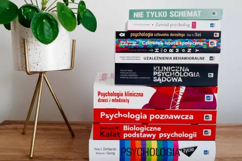 Stos książek o psychologii, w tym psychologia kliniczna, obok rośliny w doniczce.
