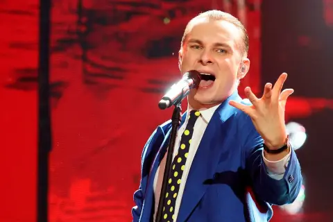 Ralph Kaminski w niebieskiej marynarce i krawacie w grochy śpiewa do mikrofonu. Jego płyty to muzyczna podróż.