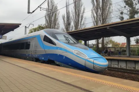 Nowoczesny eip pociąg Pendolino stoi na peronie. W tle widać wiatę, drzewa i budynki.