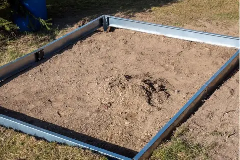 Metalowa rama wyznacza teren pod budowę szklarni. To pierwszy krok, jak zrobić fundament pod szklarnię, przygotowując podłoże.