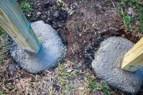 Zwei Holzpfosten werden in frisch gegossenen Beton gesetzt, um einen stabilen Zaun zu bauen. Das Einbetonieren der Pfosten sorgt für Langlebigkeit.