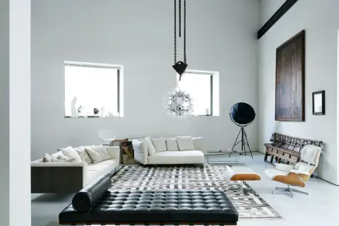 Soggiorno moderno con divani bianchi, chaise longue in pelle nera e un'iconica poltrona. Un ambiente che evoca case eleganti e raffinate.