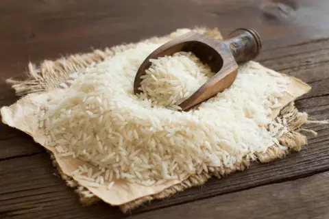 Ein Holzlöffel schöpft weißen Langkornreis aus einem Haufen auf Jute. Der Unterschied zwischen Basmati-Reis und Langkornreis ist hier visuell dargestellt.