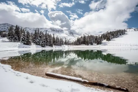 Lac d'altitude enneigé, reflétant les sapins et les montagnes. Idéal pour découvrir que faire autour de Villard de Lans en hiver.