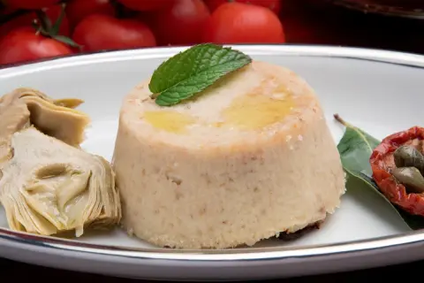 Delizioso flan di carciofi, guarnito con menta e accompagnato da carciofi sott'olio, pomodori secchi e capperi.