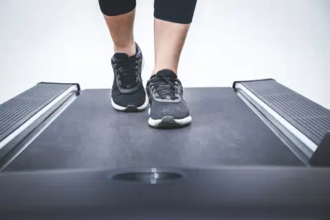 Nogi w sportowych butach stawiają pierwsze kroki na bieżni w bloku.