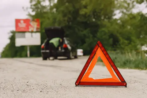 Trójkąt ostrzegawczy na drodze, obok samochodu z otwartym bagażnikiem. Awaria samochodu w terenie zabudowanym.