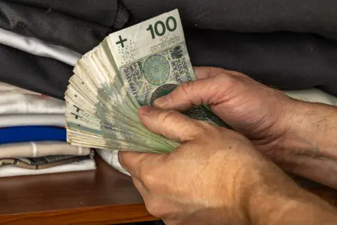 Dłonie trzymające plik banknotów 100 zł. Może to być oszczędność na przyszłość, emerytura wdowia lub po prostu wypłata.