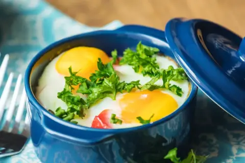 Un délicieux oeuf cocotte, deux jaunes d'œufs brillants dans leur ramequin bleu, parsemé de persil frais. Prêt à être dégusté !