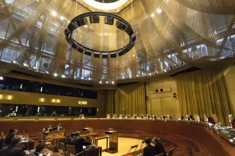 Wnętrze sali sądowej Trybunału Sprawiedliwości Unii Europejskiej, z sędziami w togach i publicznością.