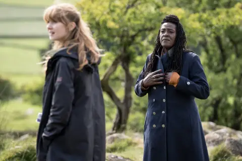 Två kvinnor i mörka rockar utomhus, en med blont hår, den andra med dreadlocks. Scen från engelska kriminalserier.