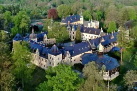 Zamek Kliczków z lotu ptaka, otoczony zielenią. Widać liczne skrzydła i wieżyczki, sugerujące bogactwo pokoi i historii.
