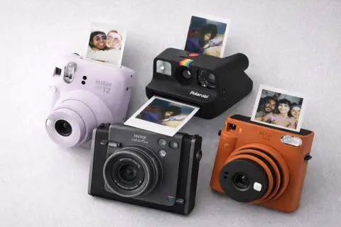 Quatre appareils photo instantanés, dont un Instax Mini 12 lilas, un Polaroid noir et un Instax orange, sortent des photos de souvenirs.