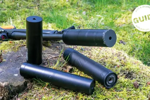 Tre ljuddämpare för jakt, en 125 mm, ligger på en mossig stubbe bredvid ett gevär. En guide hjälper dig att välja rätt.