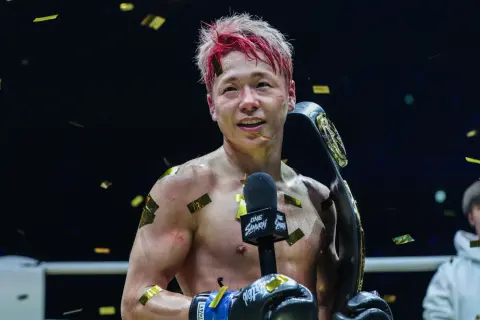 Fighter with red-streaked hair holds a championship belt, confetti falling. This victory might be the tko retirement meaning for his career.