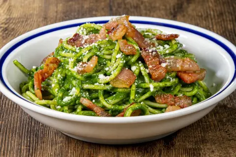 Un piatto invitante di pasta con spinaci e croccante pancetta, cosparso di formaggio grattugiato.