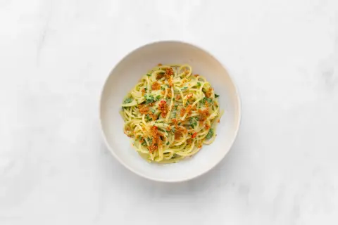 Spaghetti alla carrettiera mit frischer Petersilie, Chili und knusprigen Semmelbröseln in einer weißen Schüssel auf Marmor.
