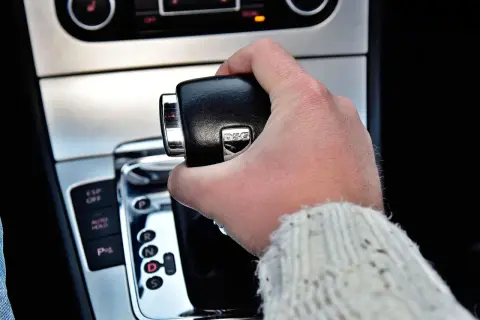 Dłoń trzymająca dźwignię zmiany biegów w samochodzie z napisem DSG. Widoczne przyciski ESP, Auto Hold i P.