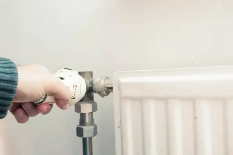Ręka reguluje termostat grzejnika w bloku, próbując poradzić sobie z zapowietrzonym grzejnikiem.