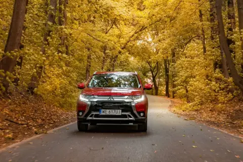 Czerwony Mitsubishi Outlander na jesiennej drodze wśród złotych liści. Sprawdź jego spalanie w podróży!