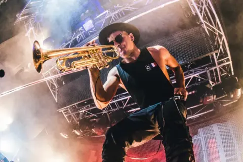Timmy Trumpet gra na trąbce na scenie w Polsce, otoczony dymem i światłami.