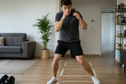 Man practicing boxing steps in his living room, with a couch and plant in the background.