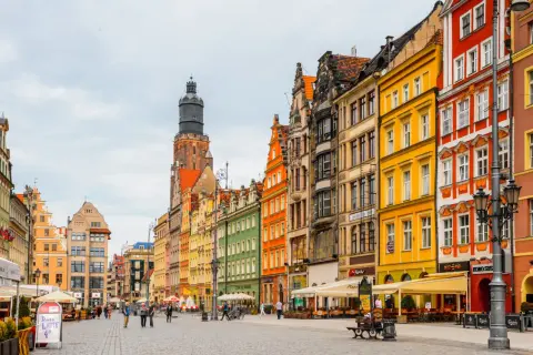 Bunte Häuserfronten am Wroclaw Rynek, mit einem markanten Turm im Hintergrund. Menschen spazieren über den gepflasterten Platz.