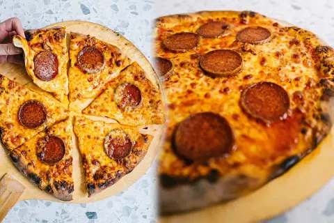 En hand tar en bit av en klassisk neapel pizza med pepperoni och smält ost.