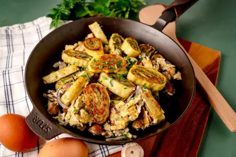 Herzhafte Maultaschen-Pfanne mit Rührei, Zwiebeln und frischen Kräutern, appetitlich in einer Gusseisenpfanne serviert.