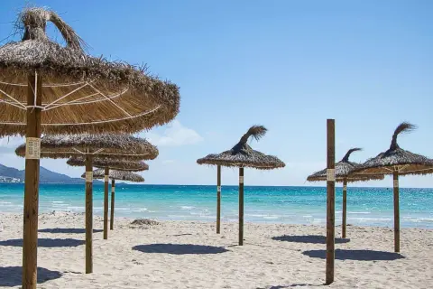 Słomiane parasole na piaszczystej plaży nad turkusową wodą, idealne na wakacje w zatoce alkudyjskiej.