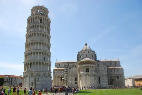 La Torre di Pisa si può salire, con la cattedrale sullo sfondo. Turisti ammirano la celebre struttura pendente sotto un cielo azzurro.