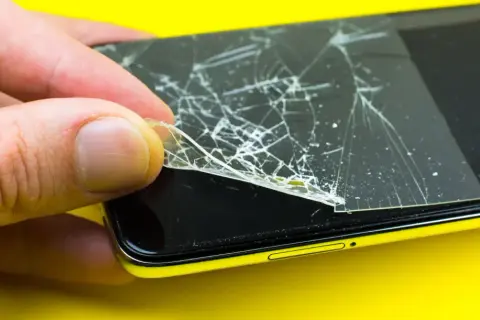 Dłoń zdejmuje pęknięte szkło hartowane 9h z ekranu telefonu.