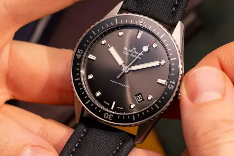 Manos ajustando un reloj automático Blancpain Fifty Fathoms Bathyscaphe con correa de tela negra.