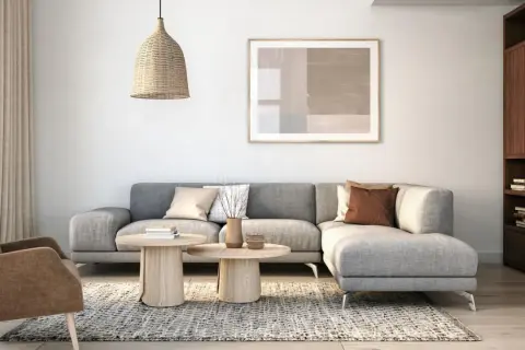Gemütliches Wohnzimmer mit grauem Sofa, beigefarbenem Sessel, Holztischen und einem Bücherregal. Modernes interior design.