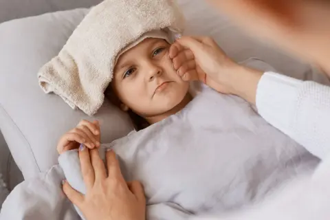 Dziecko z gorączką i okładem na głowie. Matka troskliwie dotyka czoła, zastanawiając się, dlaczego ocet zbija gorączkę.