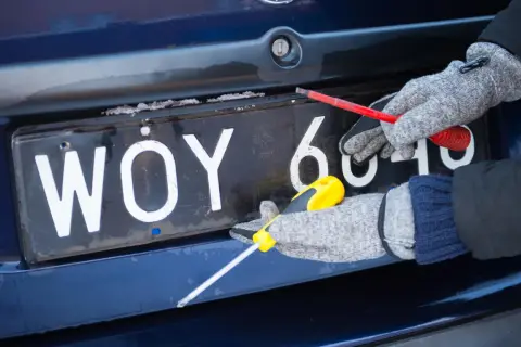 Ręce w rękawiczkach odkręcają śruby tablicy rejestracyjnej.