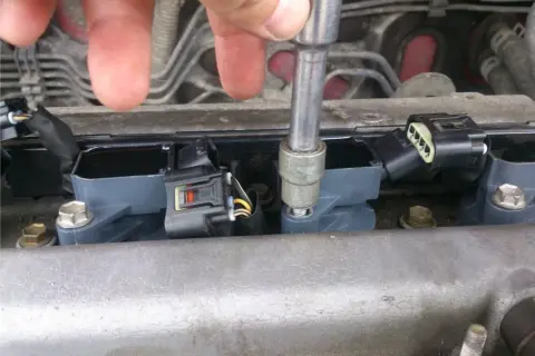 Naprawa Opla z błędem dtc p0301. Mechanik dokręca cewkę zapłonową kluczem nasadowym.