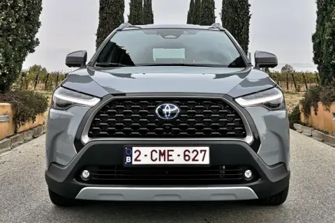 Szary SUV Toyota Hybryda 2022 z przodu, z grillem i światłami LED, na tle winnicy i drzew.