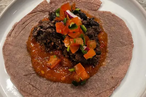 En lila tortilla med en klick refried beans, toppad med salsa och hackad lök.