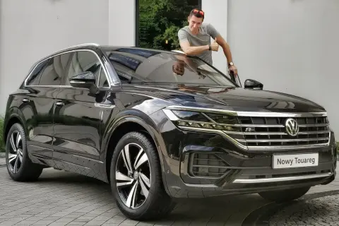 Mężczyzna z kciukiem w górę przy nowym, czarnym Volkswagenie Touareg. Jego imponujące wymiary robią wrażenie.