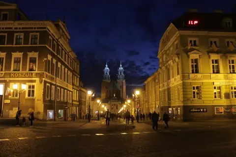 Wieczorne Gniezno: oświetlona ulica prowadzi do katedry, a budynki po bokach tworzą malowniczy widok. Atrakcje miasta nocą zachwycają.