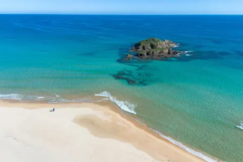 Pusta plaża na Costa Smeralda, z turkusową wodą i samotną postacią spacerującą brzegiem.