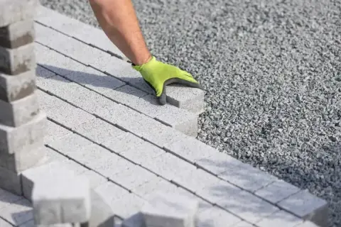 Dłoń w zielonej rękawicy układa kostkę brukową na podsypce. Właściwe podsypka pod kostkę brukową proporcje to klucz do trwałej nawierzchni.